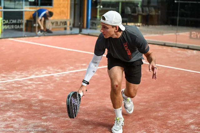 A player in a white cap reaching low for a backhand