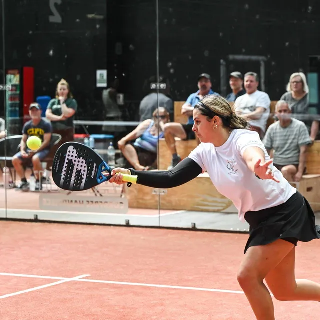 A player stretching for a low forehand with spectators behind the glass