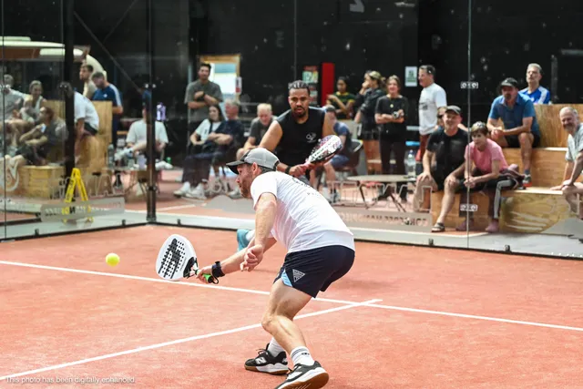 A player bending low for a backhand volley in front of the crowd