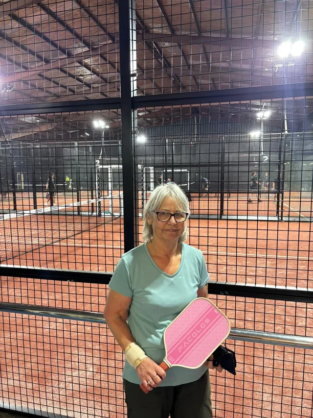 A member holding a pink pickleball paddle beside the courts