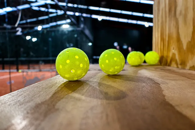 Pickleballs lined up on a wooden ledge beside the court