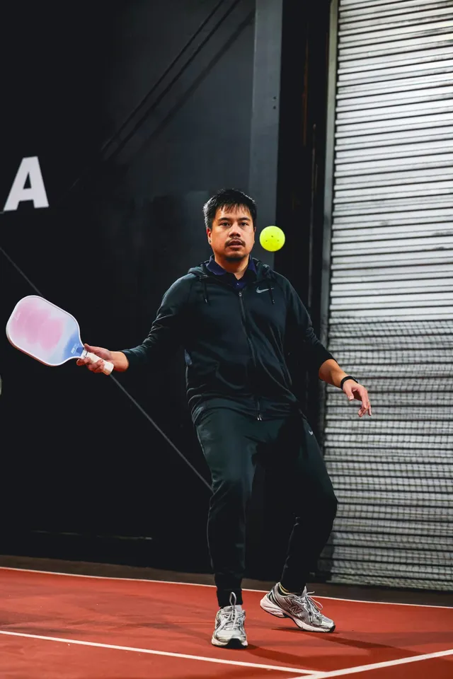 A pickleball player reaching for the ball with a pink paddle