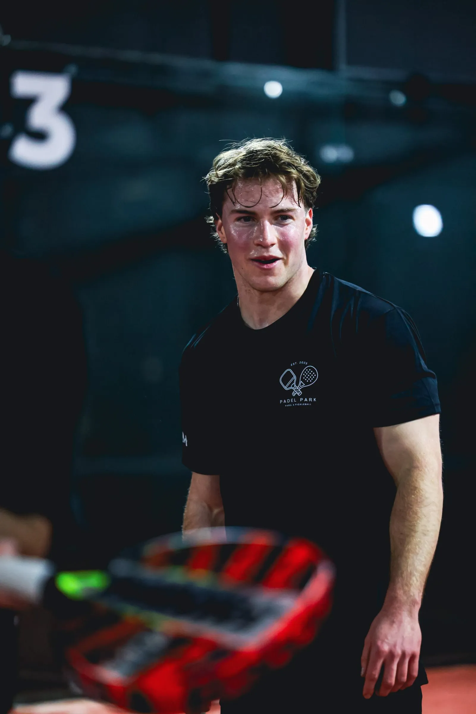 A Padel Park team member in the team tee, smiling on court