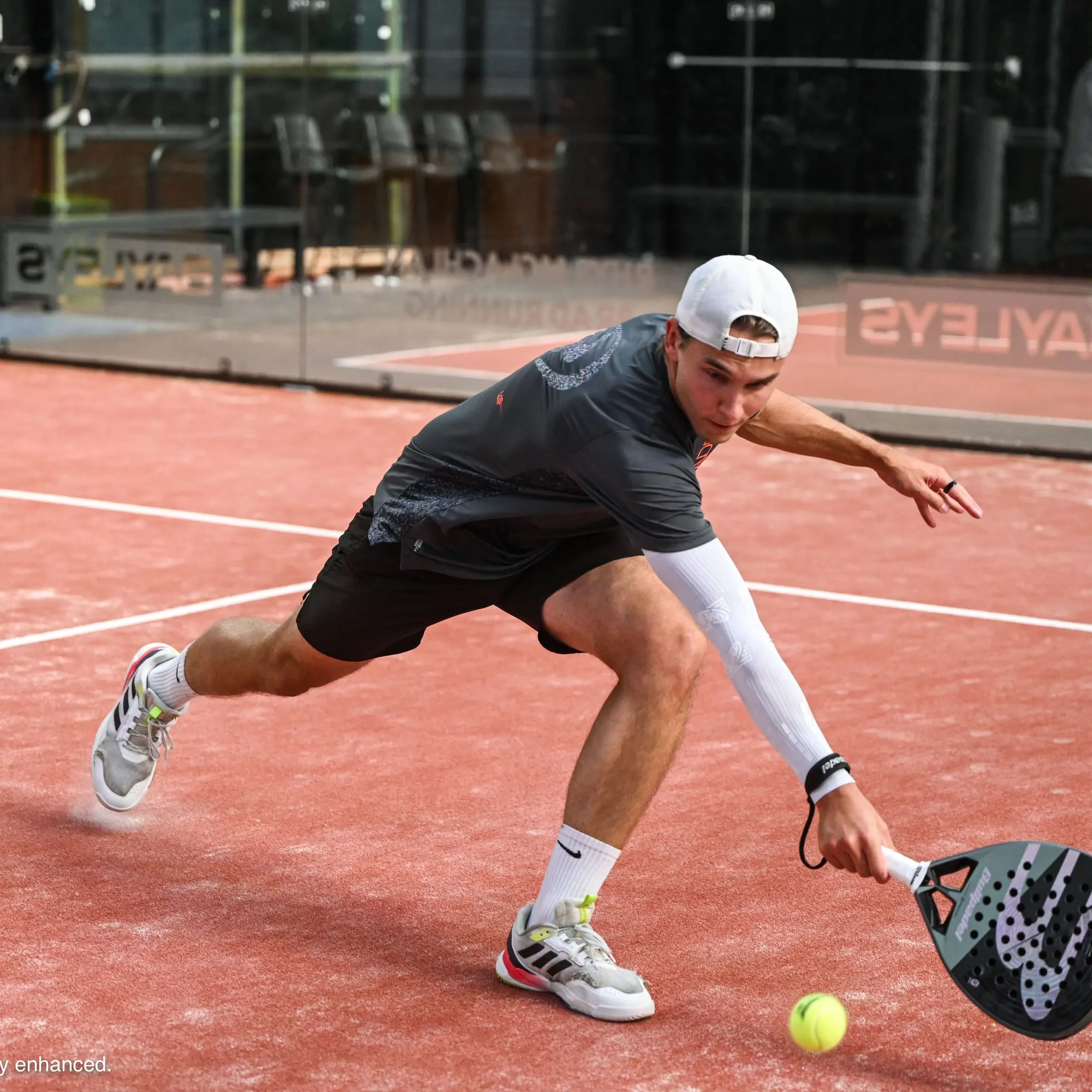 A padel player reaching low for a ball on court